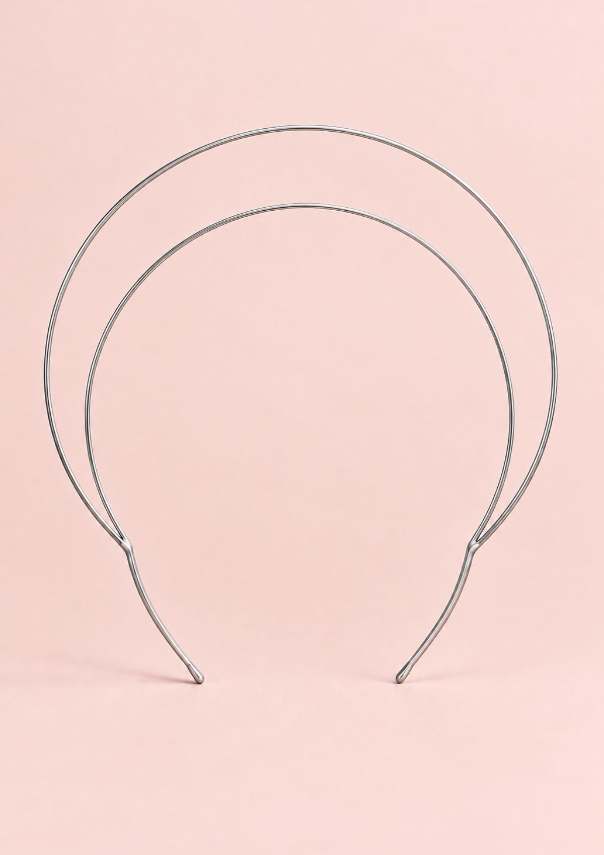 Silver halo crown headband with a minimalist double-loop metal design on a pale pink background.