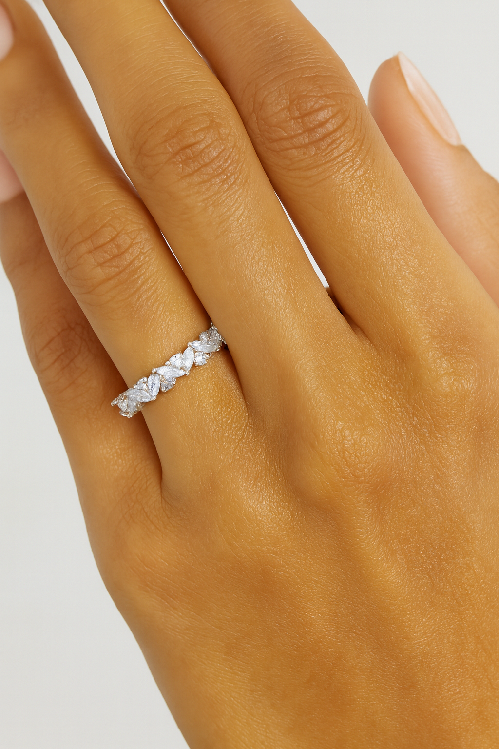 Silver ring with small stones on a hand against a neutral background