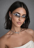 Load image into Gallery viewer, Woman wearing sunglasses and a white top against a gray background
