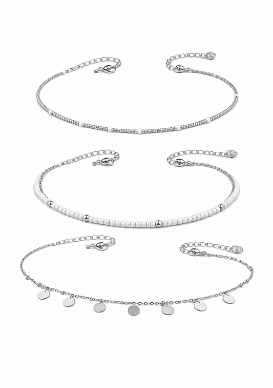 Three silver-toned delicate chain necklaces with different bead and disc charm designs, arranged vertically on a plain white background.