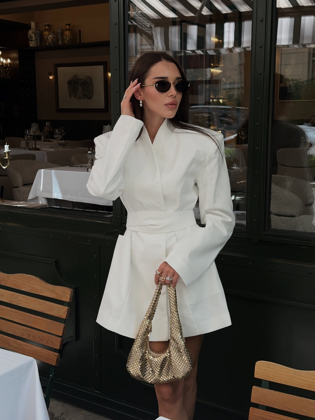 Woman in a white coat dress holding a handbag in an outdoor setting.