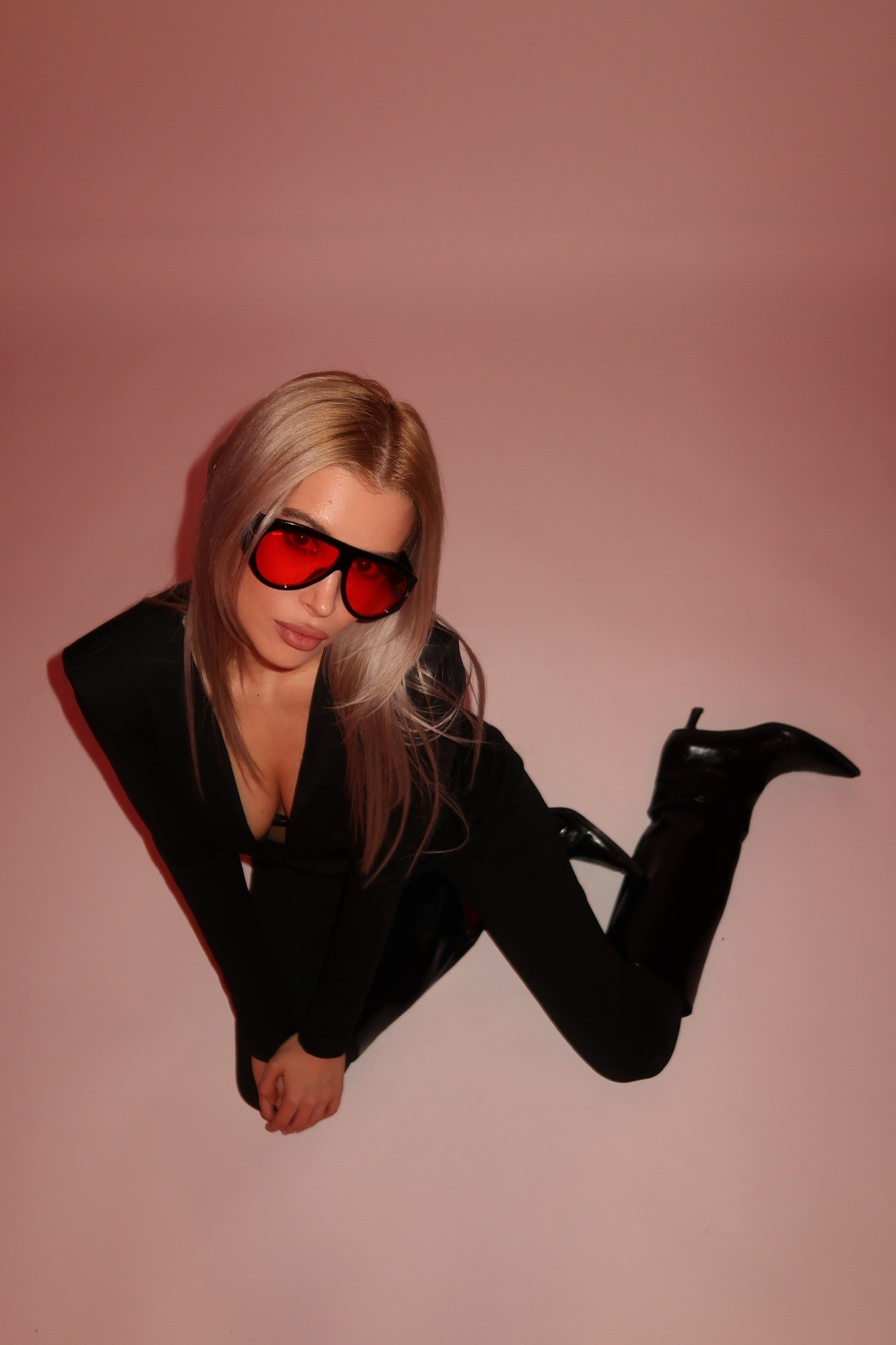 Person wearing a black outfit and red sunglasses on a pink background