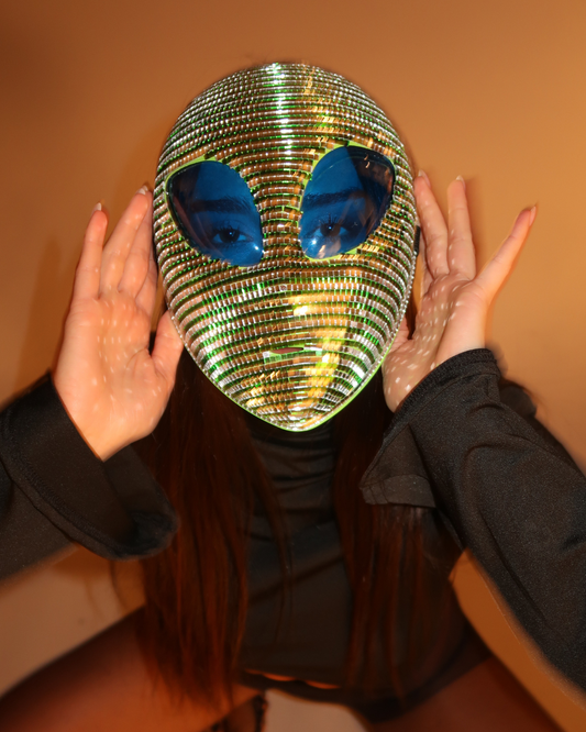 Person wearing a reflective alien mask with blue eyes against a plain background