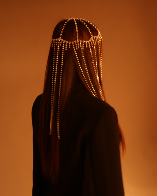 Person wearing a beaded headpiece against an orange background