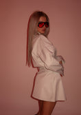 Load image into Gallery viewer, Woman wearing a beige set outfit and red sunglasses against a pink background
