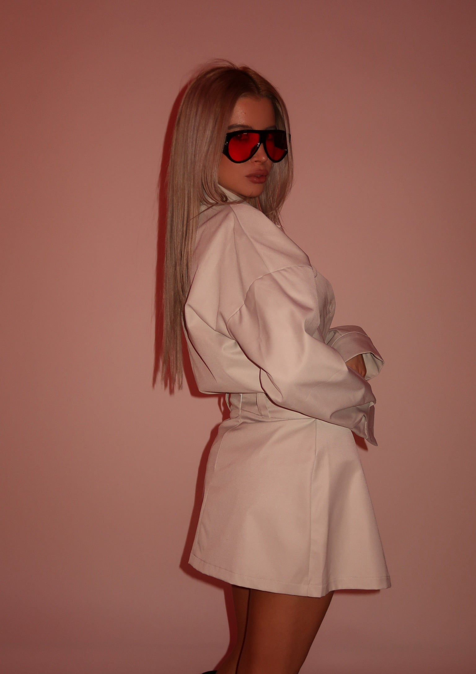 Woman wearing a beige set outfit and red sunglasses against a pink background