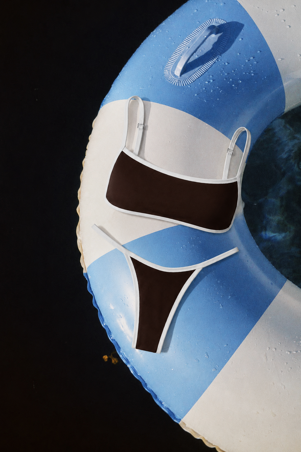 A close-up of a blue and white striped inflatable pool float with a bikini top and bikini bottom attached, shown against a dark background.