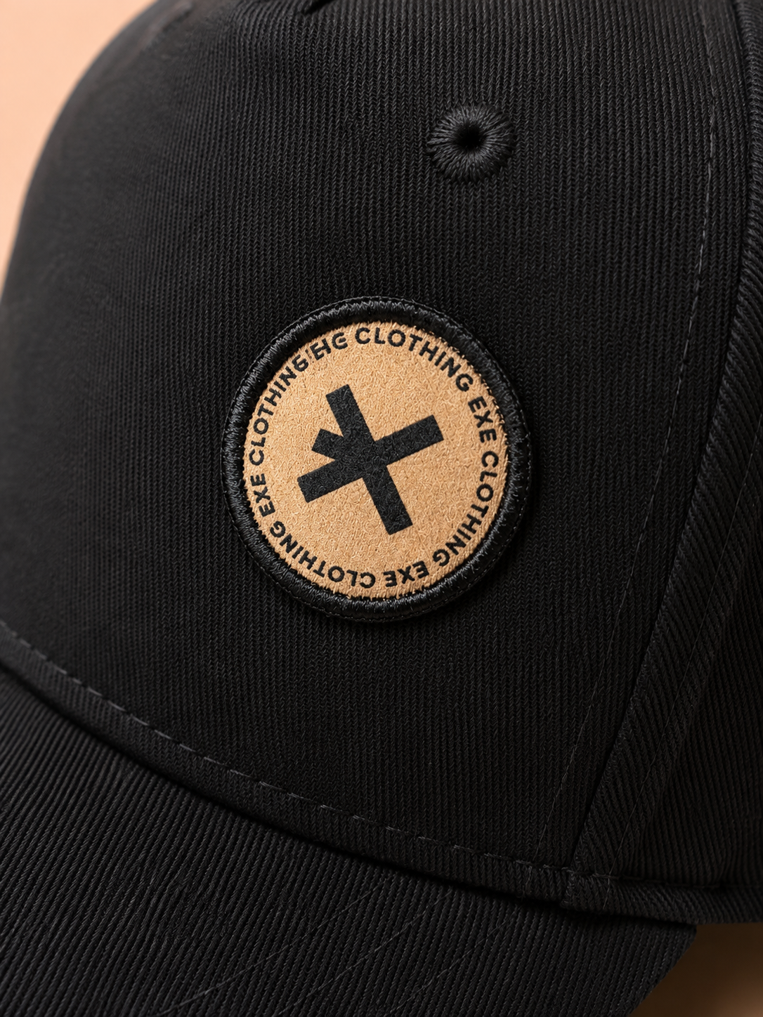 Close-up of a black baseball cap featuring a circular embroidered patch on the front. The patch is beige with a black embroidered cross in the center and the text 'EXE CLOTHING' embroidered around the border.