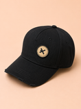 Заредете изображението в програмата за преглед на галерия, A black distressed baseball cap with a circular beige patch featuring a black 'X' logo on the front, set against a solid peach background.
