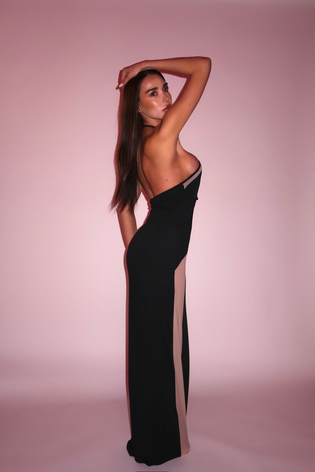 Woman wearing a black evening gown with sheer panels on a pink background