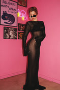 Load image into Gallery viewer, A model wearing a black knitted dress with long sleeves, standing in a room with pink walls and colorful decorations.

