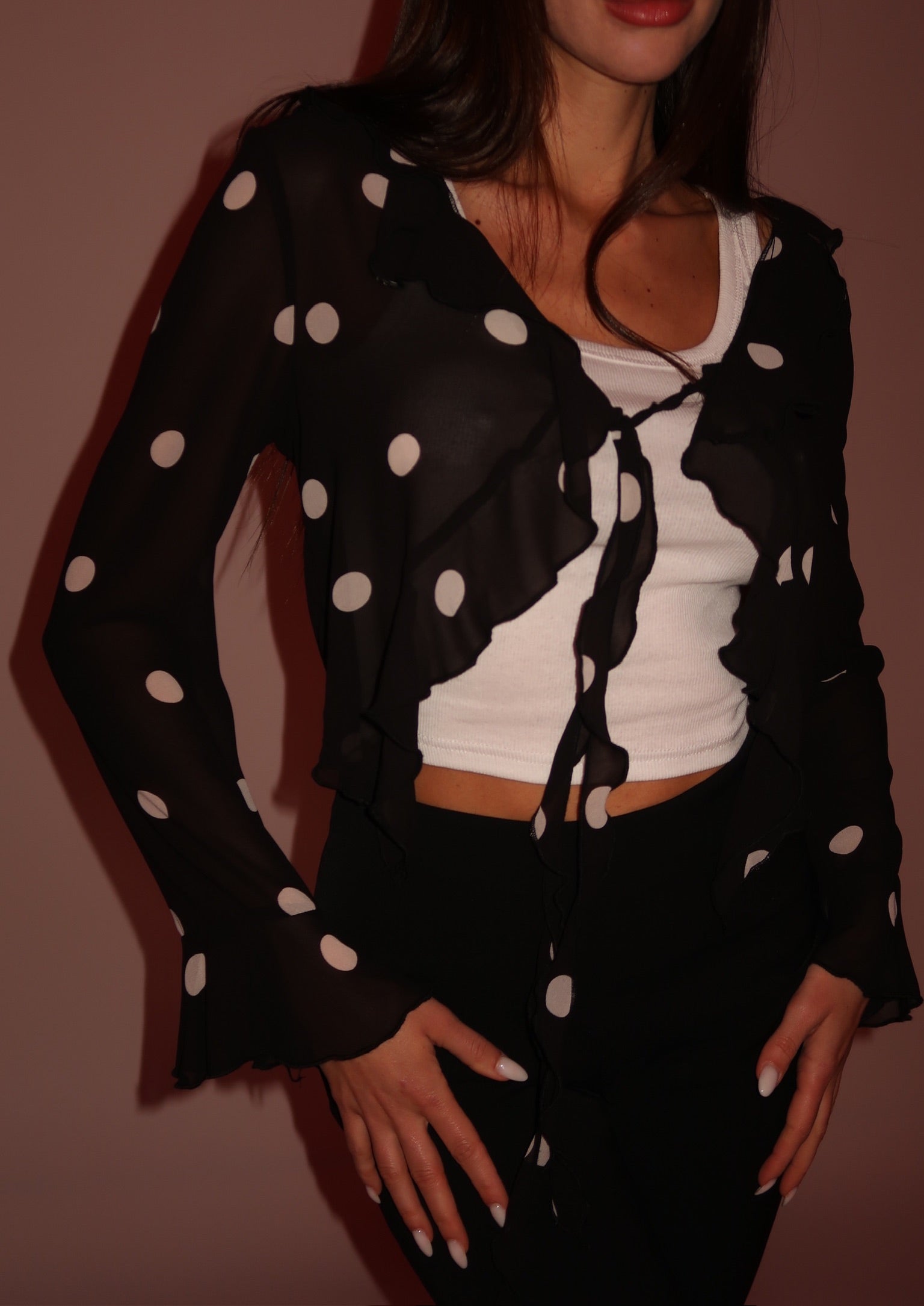 Person wearing a black polka dot outfit with a white top against a brown background