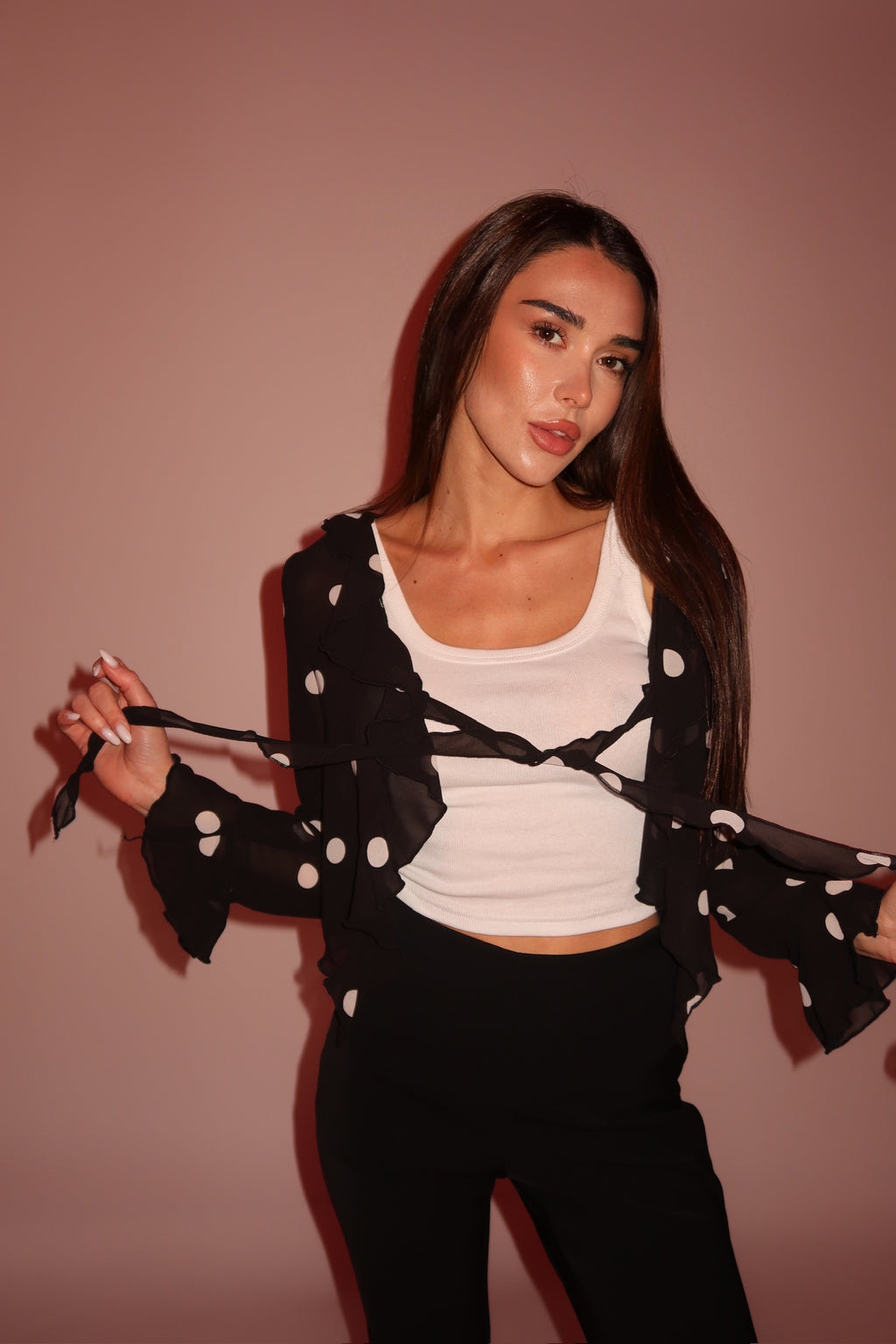 Woman wearing a black polka dot top over a white top with a plain background