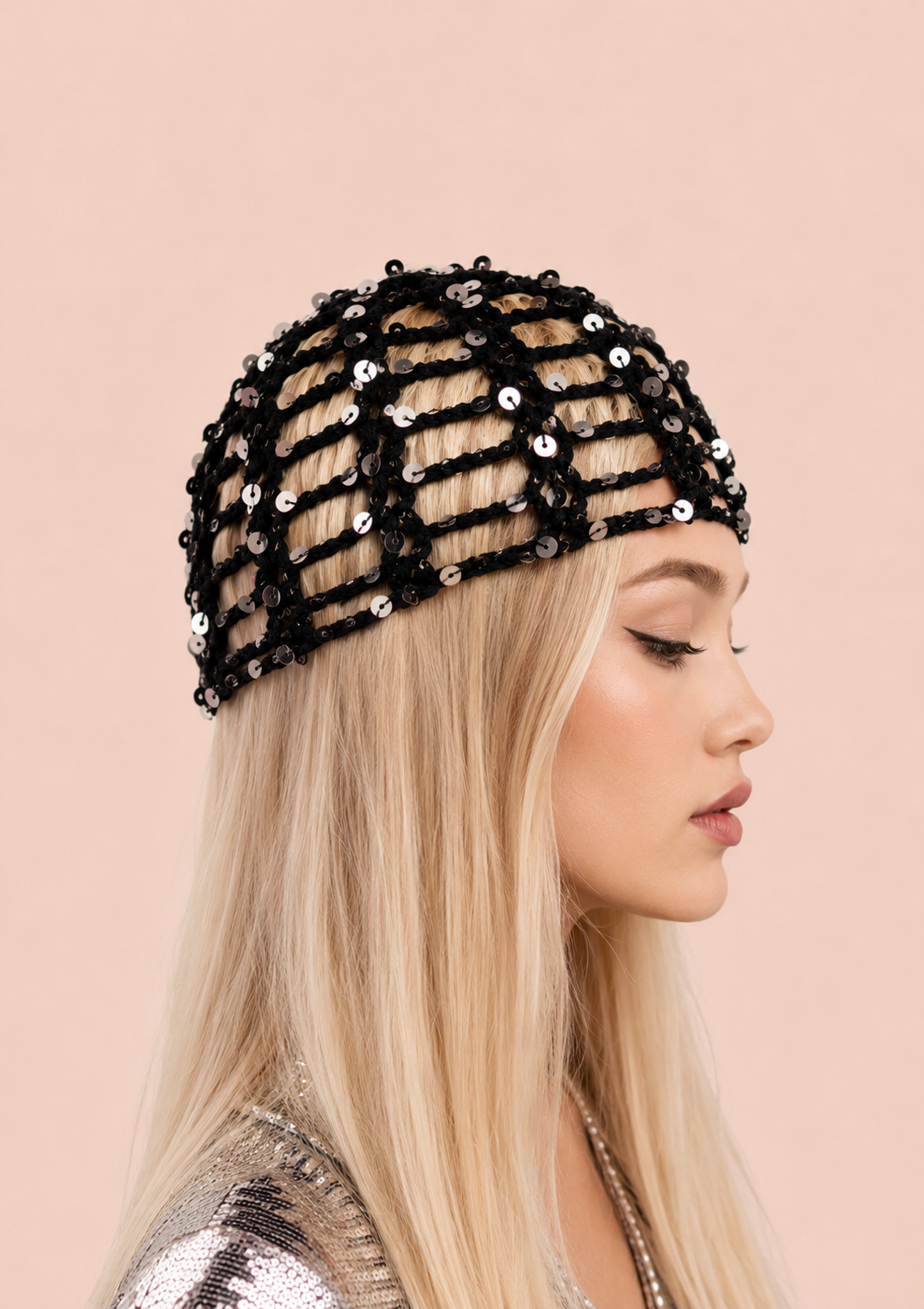 A blonde woman in profile wearing a black sequined mesh hat against a solid pale pink background.