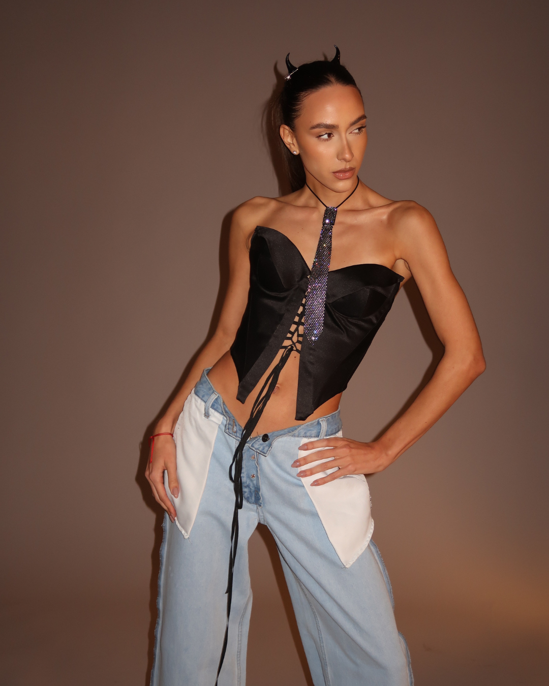 Model wearing a black strapless top and tie and light blue jeans against a brown background