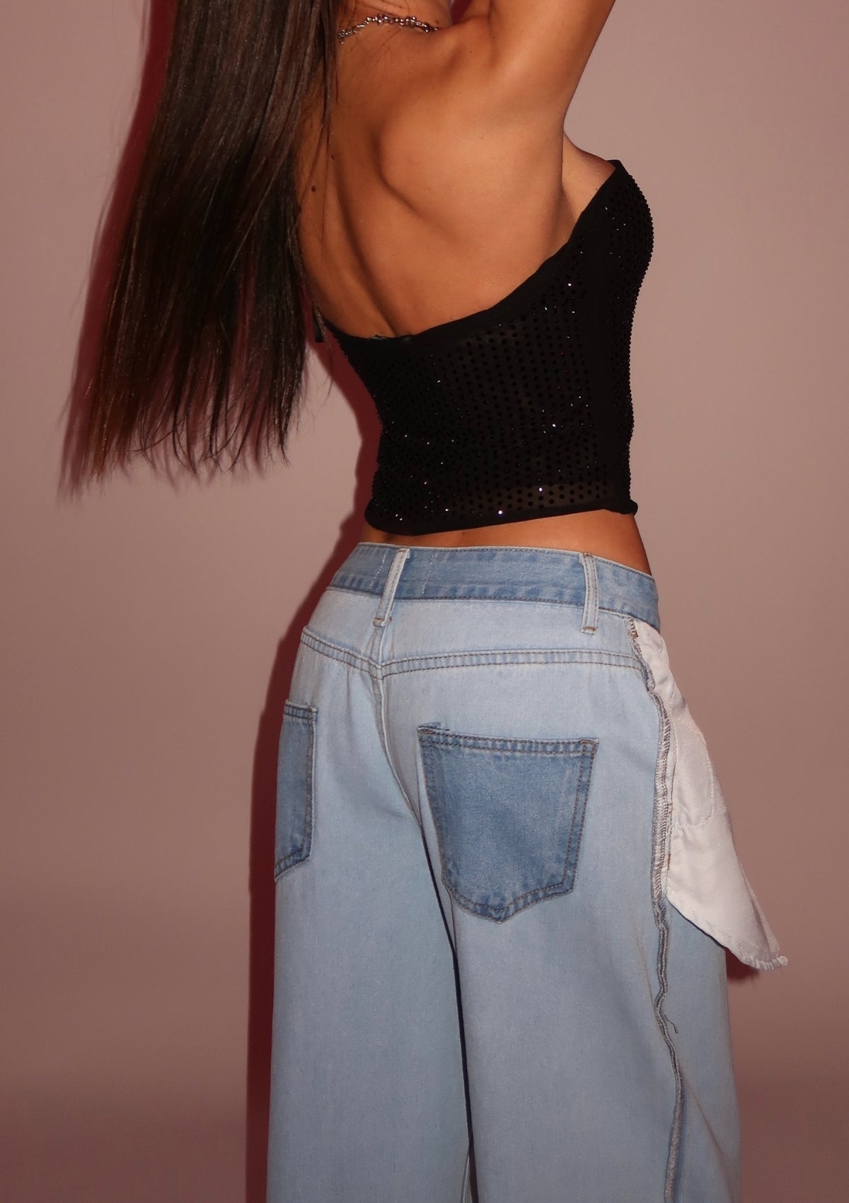 Person wearing a black crop top and light blue jeans against a beige background