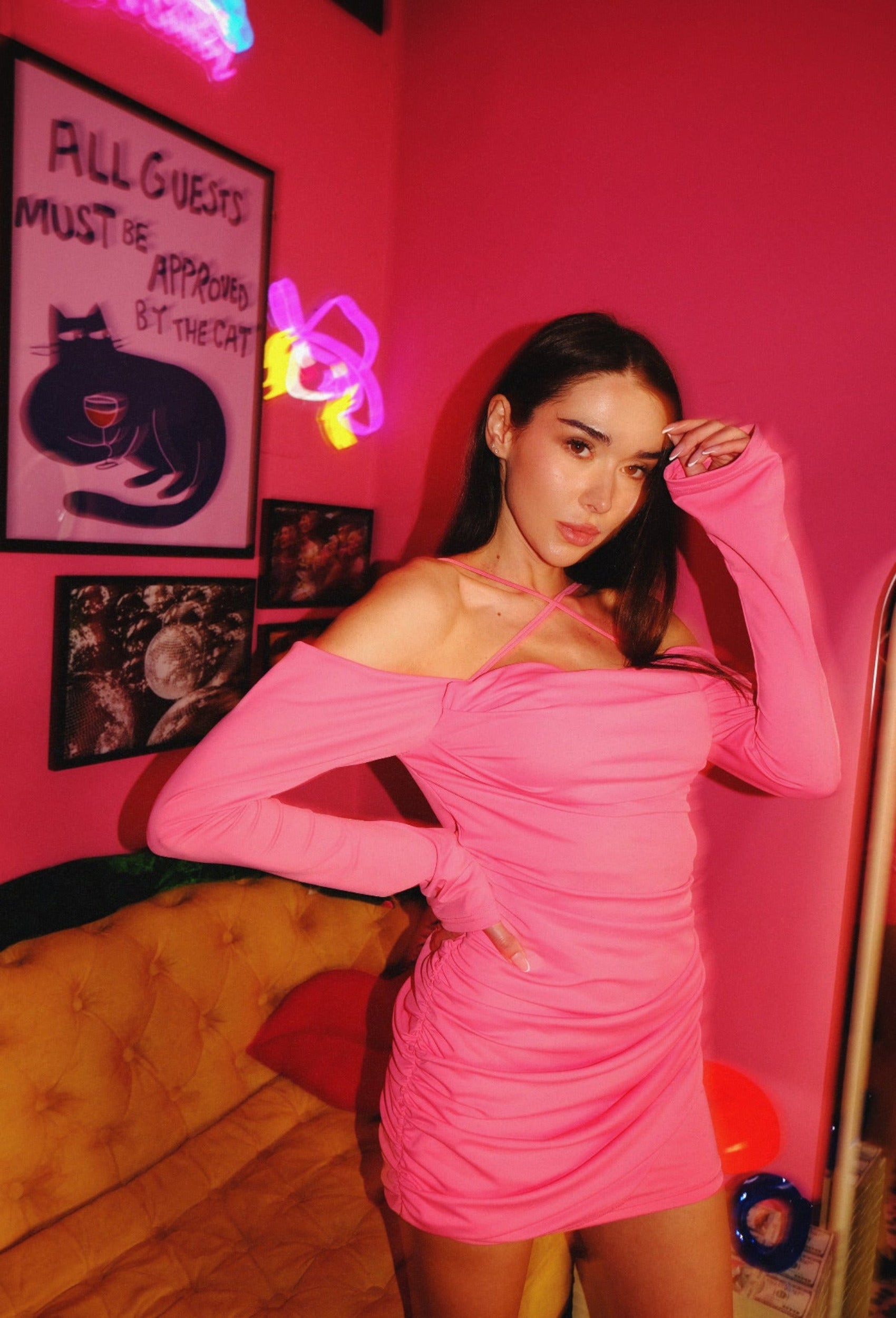 Woman in a bright pink dress standing in a room with pink walls.