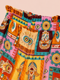 Заредете изображението в програмата за преглед на галерия, A close-up of a colorful patchwork shorts featuring bohemian Hamsa hand and eye motifs in orange, pink, yellow, teal, and brown on a solid pale peach background.
