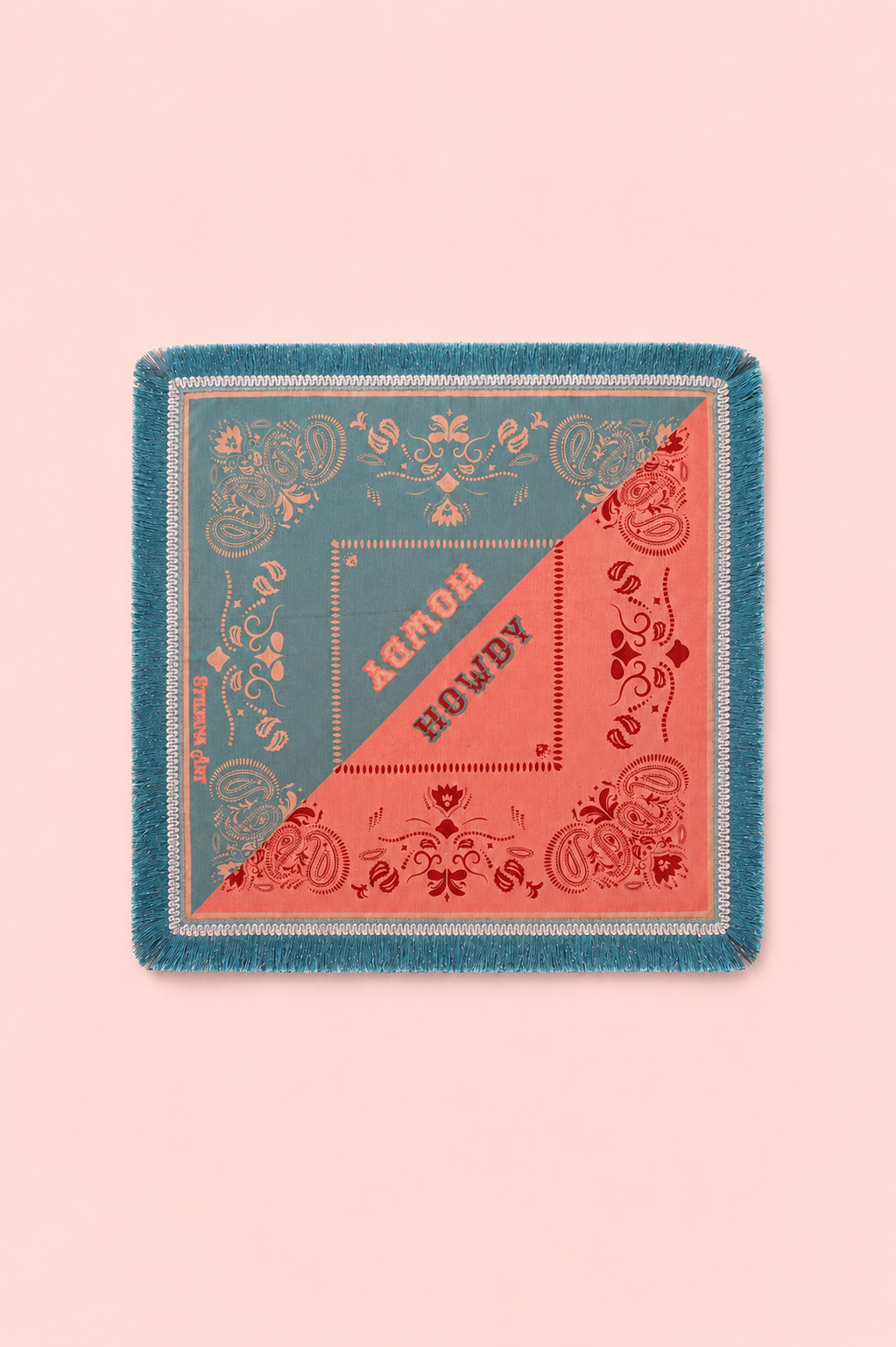 A square fringed scarf laid flat on a solid pale pink background. The scarf features a split design with teal blue on one side and coral pink on the other, decorated with ornate floral patterns and the words 'ALMOST HOWDY' printed diagonally across the center.