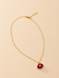 A gold chain necklace with a small red lips pendant featuring white teeth, displayed on a light beige background.