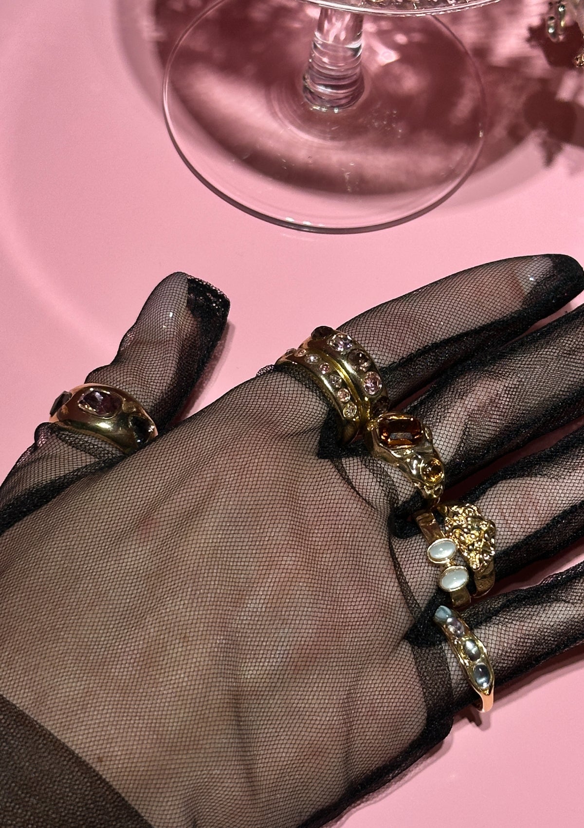Hand wearing a gold rings with gemstones on a pink surface