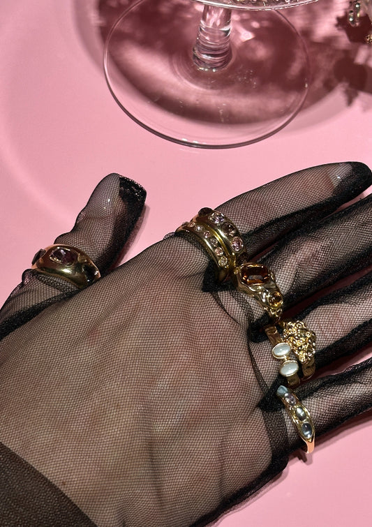 Hand wearing a gold rings with gemstones on a pink surface