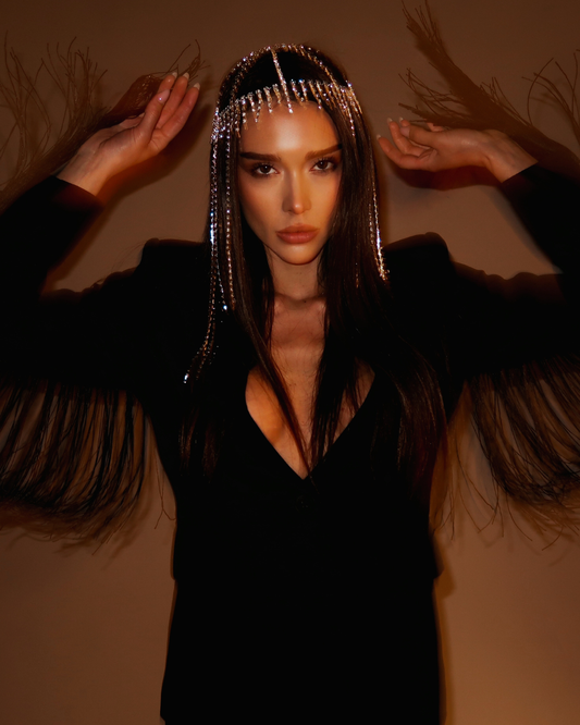 Woman wearing a feathered black garment with a decorative headpiece against a warm-toned background