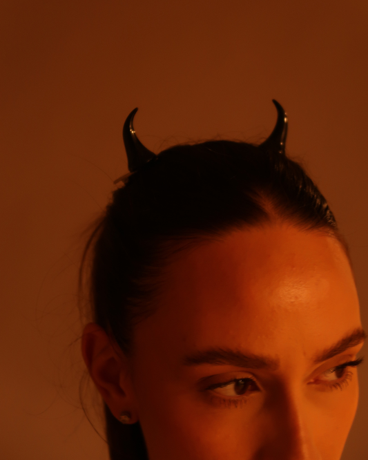 Person wearing small devil horns hairpins against a warm-toned background