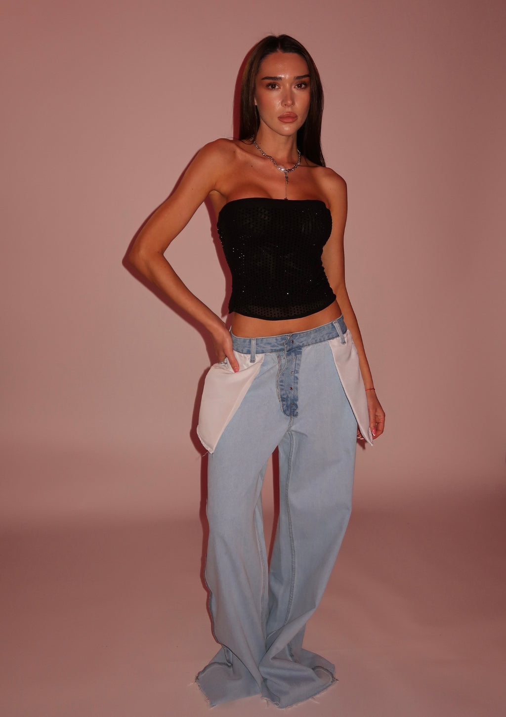 Woman wearing a black strapless top and light blue jeans against a pink background