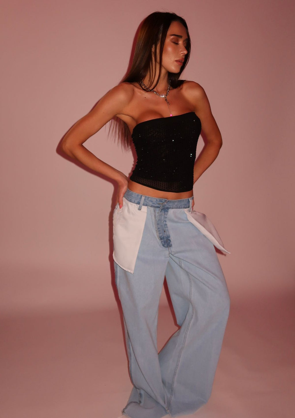 Woman wearing a black strapless top and light blue pants against a pink background