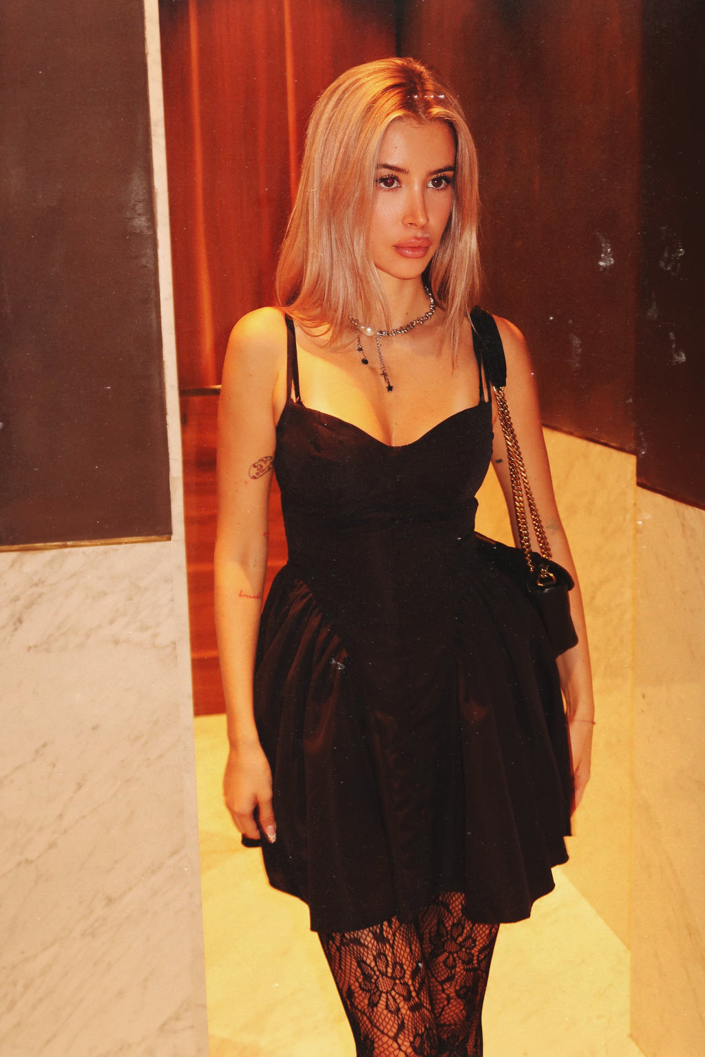 Woman wearing a black dress with sheer sleeves against a textured wall.