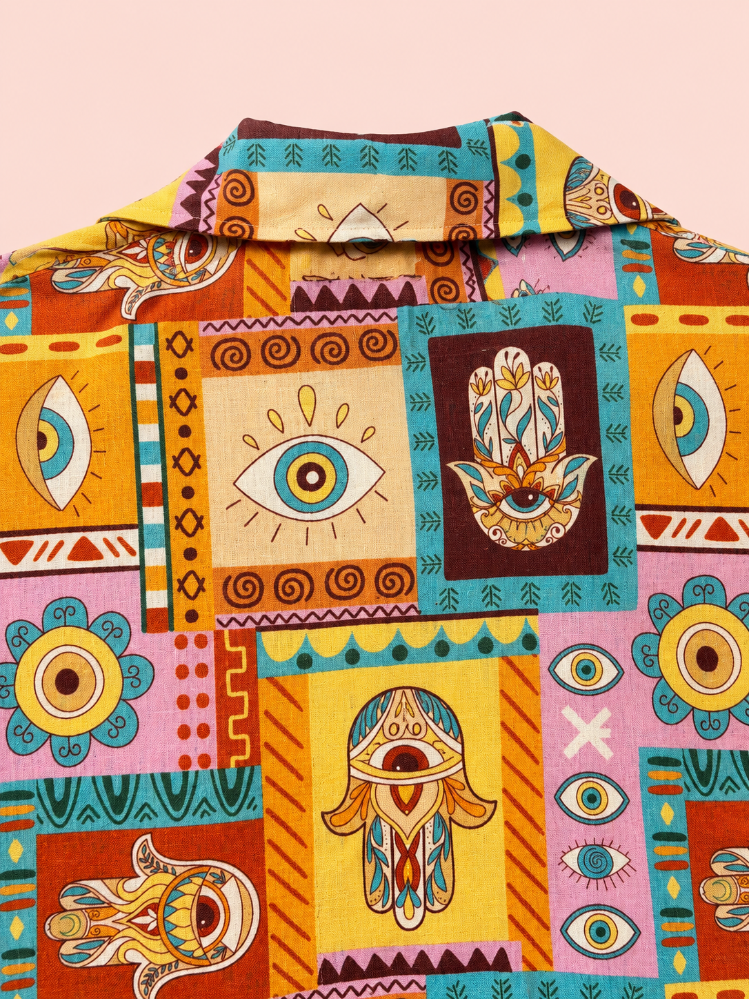 A close-up of a collared button-up shirt featuring a vibrant, multicolored patchwork print with Hamsa hands, evil eye motifs, and tribal geometric patterns in yellow, orange, teal, pink, and brown.