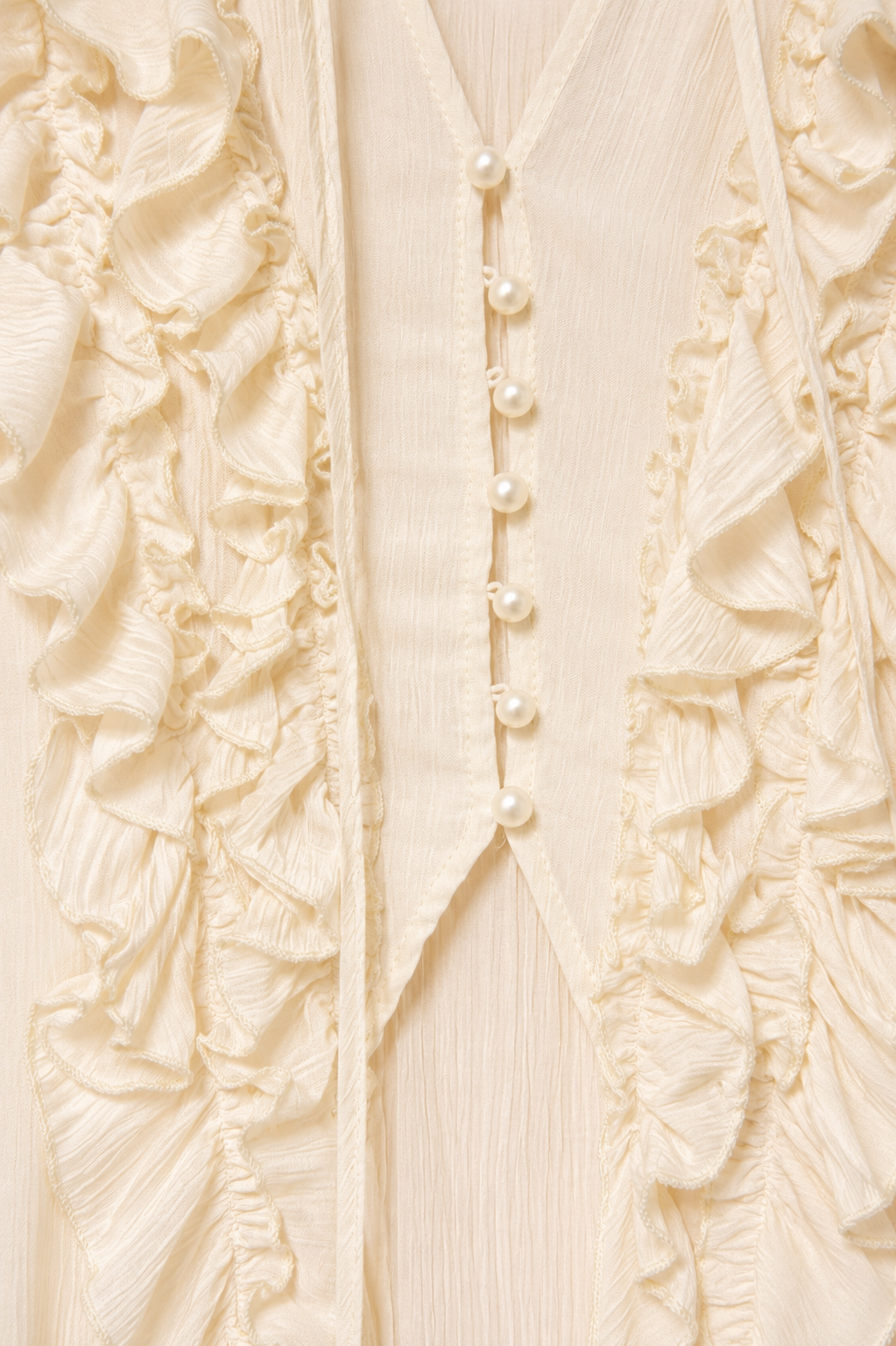 Close-up of a cream-colored textured fabric garment featuring vertical ruffles on both sides and a central V-neckline accented with a row of small pearl-like buttons.