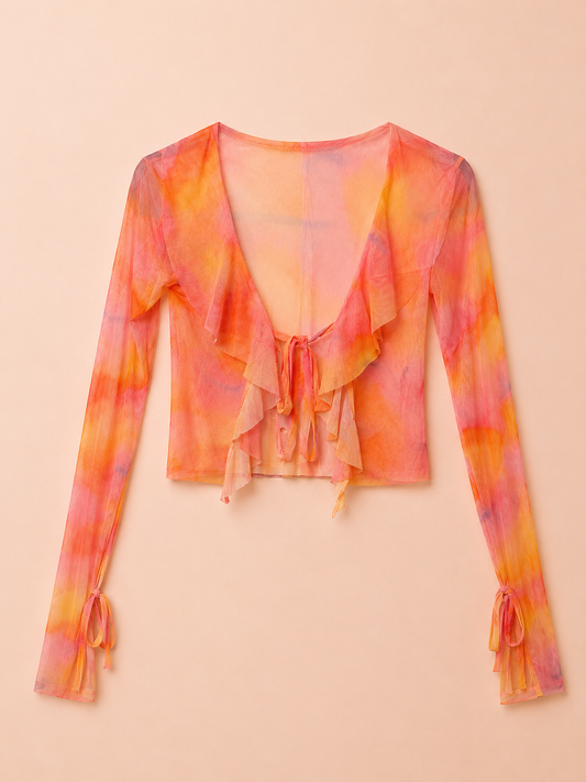 A long-sleeve sheer mesh crop top with a ruffled V-neckline and tie-front detail, featuring a vibrant orange, pink, and yellow tie-dye pattern, laid flat on a light beige background.