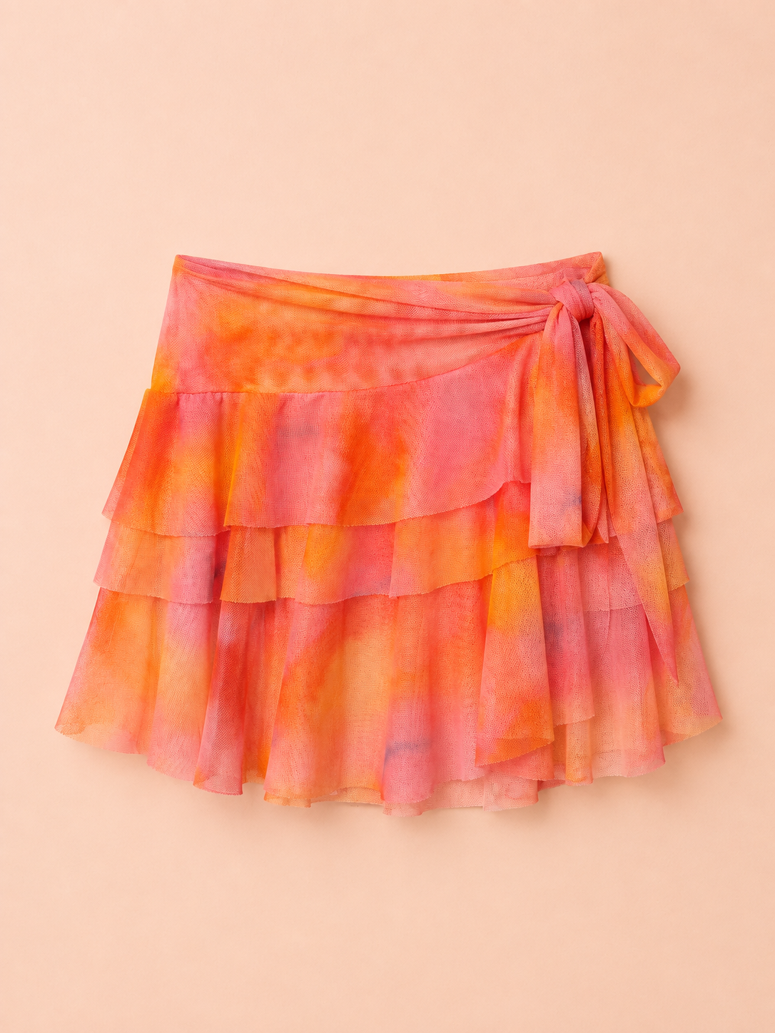 A tiered ruffle wrap skirt in a vibrant orange and pink tie-dye pattern, featuring a side tie closure, laid flat on a solid peach background.