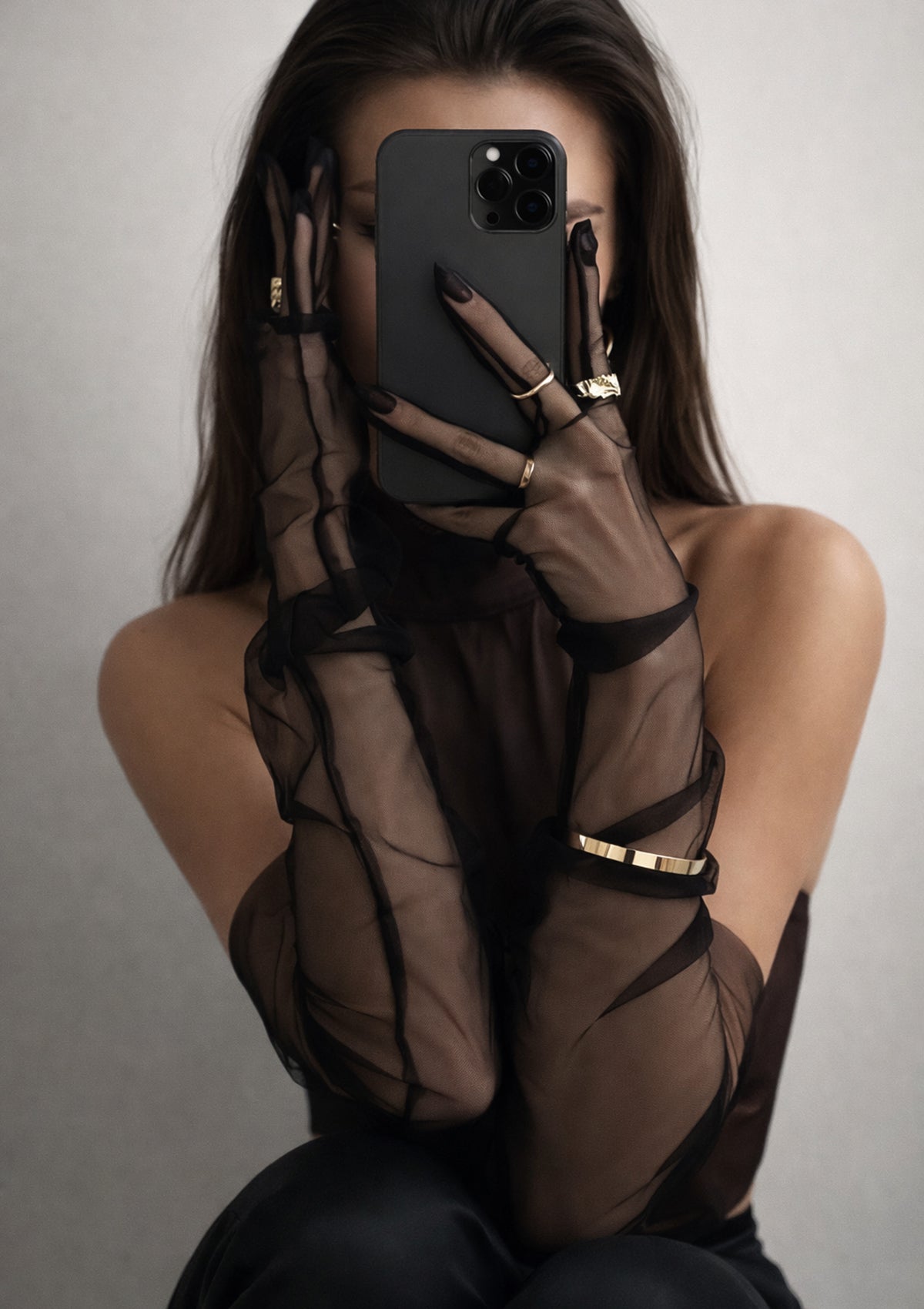 Person wearing a sheer black gloves with gold accents, holding a phone.