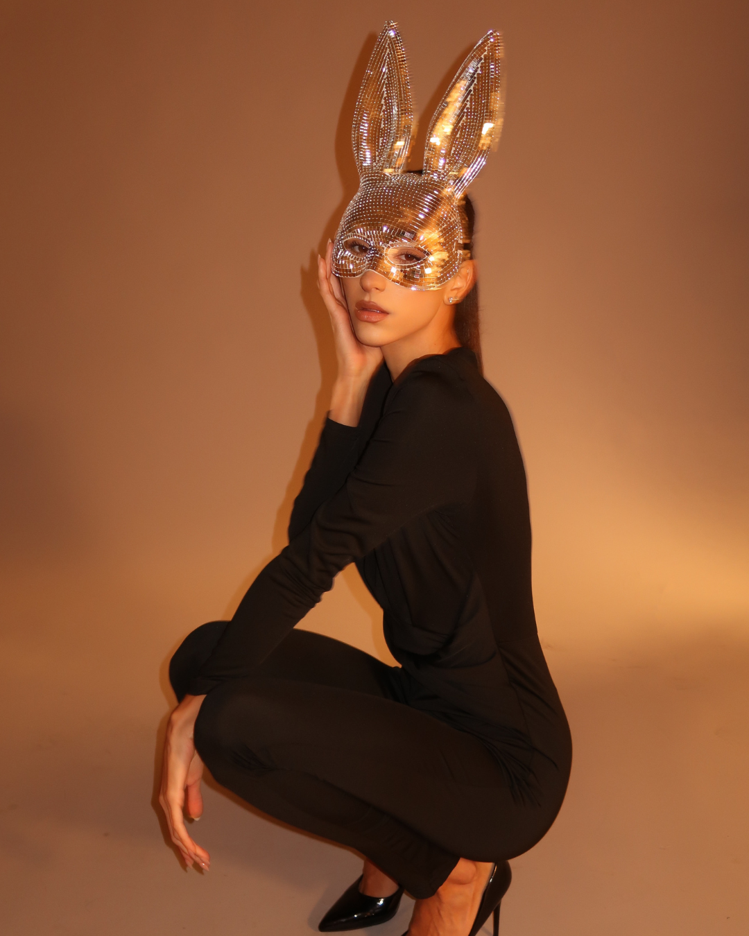 Person wearing a sparkling bunny mask against a brown background