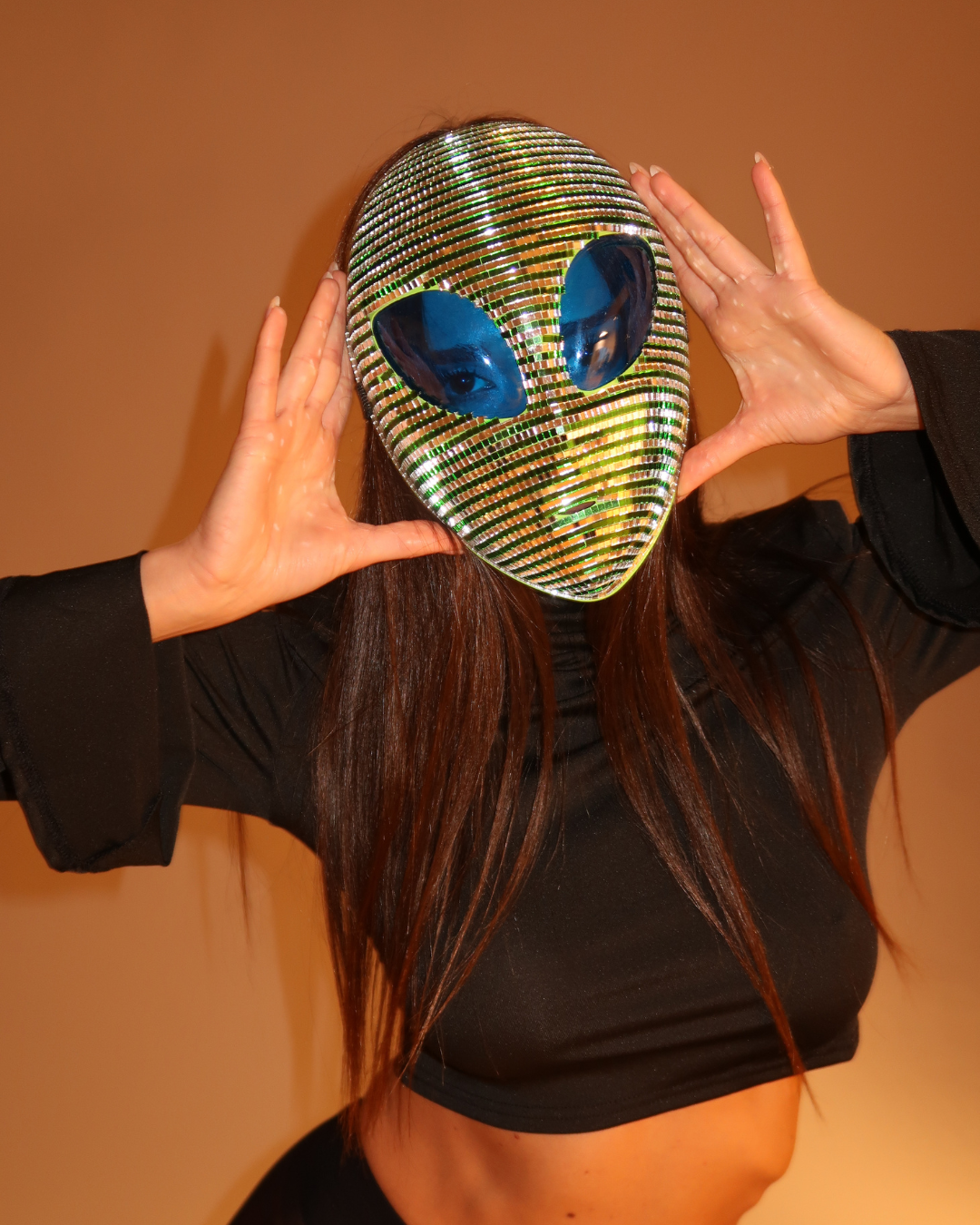 Person wearing a sparkling alien mask with blue eyes against a brown background