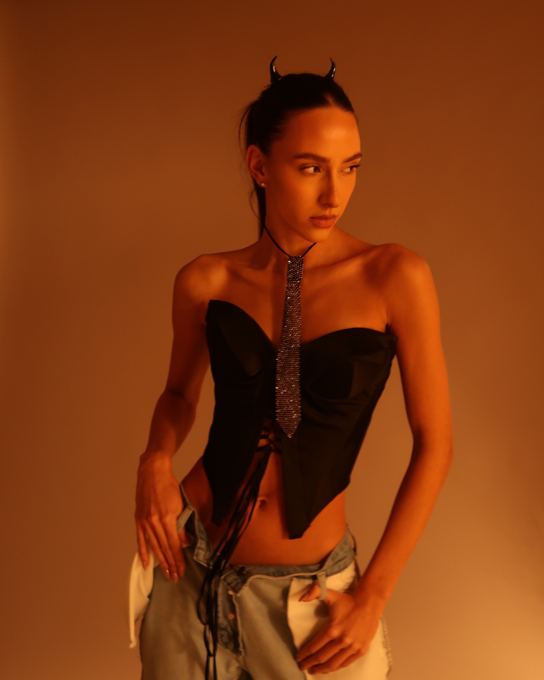 Person wearing a black strapless top with a tie and light-colored pants against an orange background