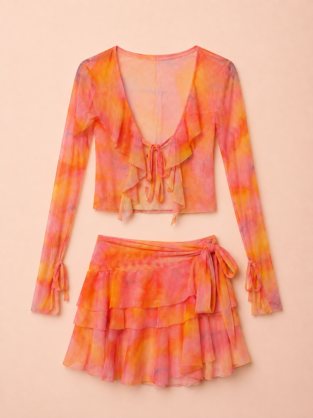 A two-piece women's outfit set featuring a long-sleeve ruffled crop top and a matching tiered ruffled mini skirt, both in a vibrant orange and pink tie-dye pattern, displayed against a solid pale peach background.