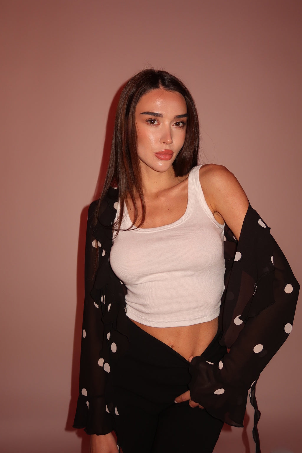 Woman wearing a white tank top and black polka dot cover-up against a brown background