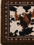Заредете изображението в програмата за преглед на галерия, A close-up of a woven scarf with fringe, featuring a brown and cream cow-print center surrounded by a dark brown border with geometric motifs and text reading 'STILL LIFE ART' and 'WILD WEST LOOKS GOOD ON ME'.
